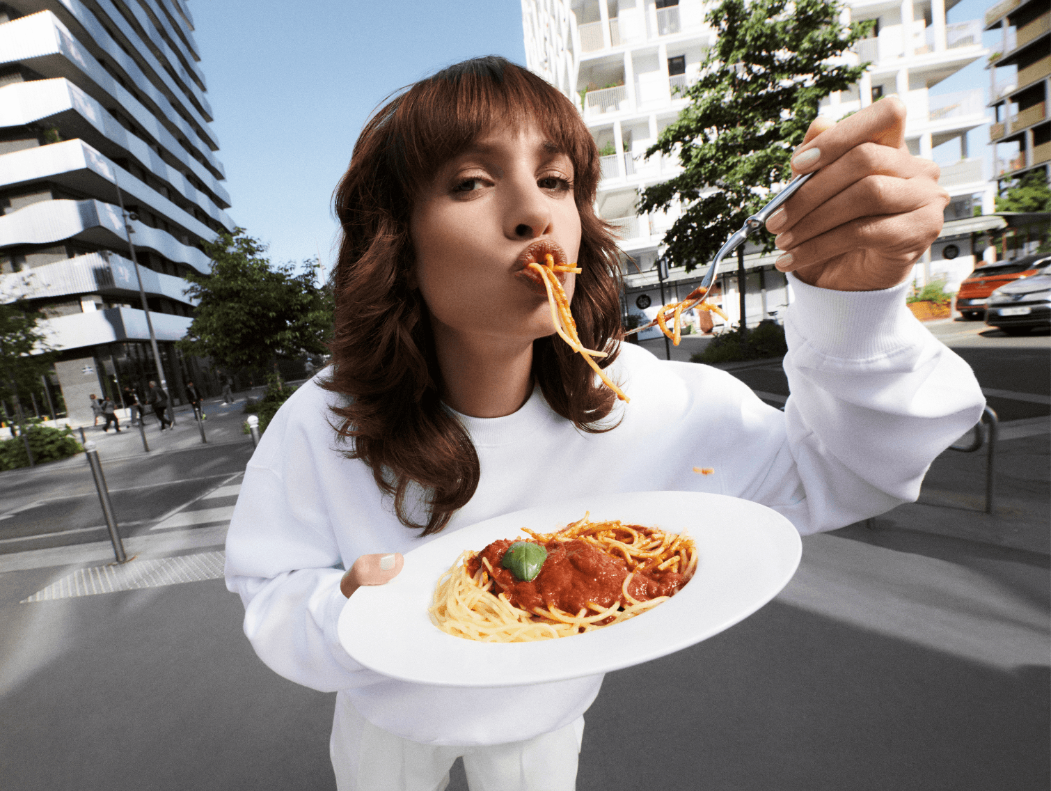 femme avec un pull blanc et une coupe de cheveux wolf cut mangeant des pates à la bolognaise à Paris